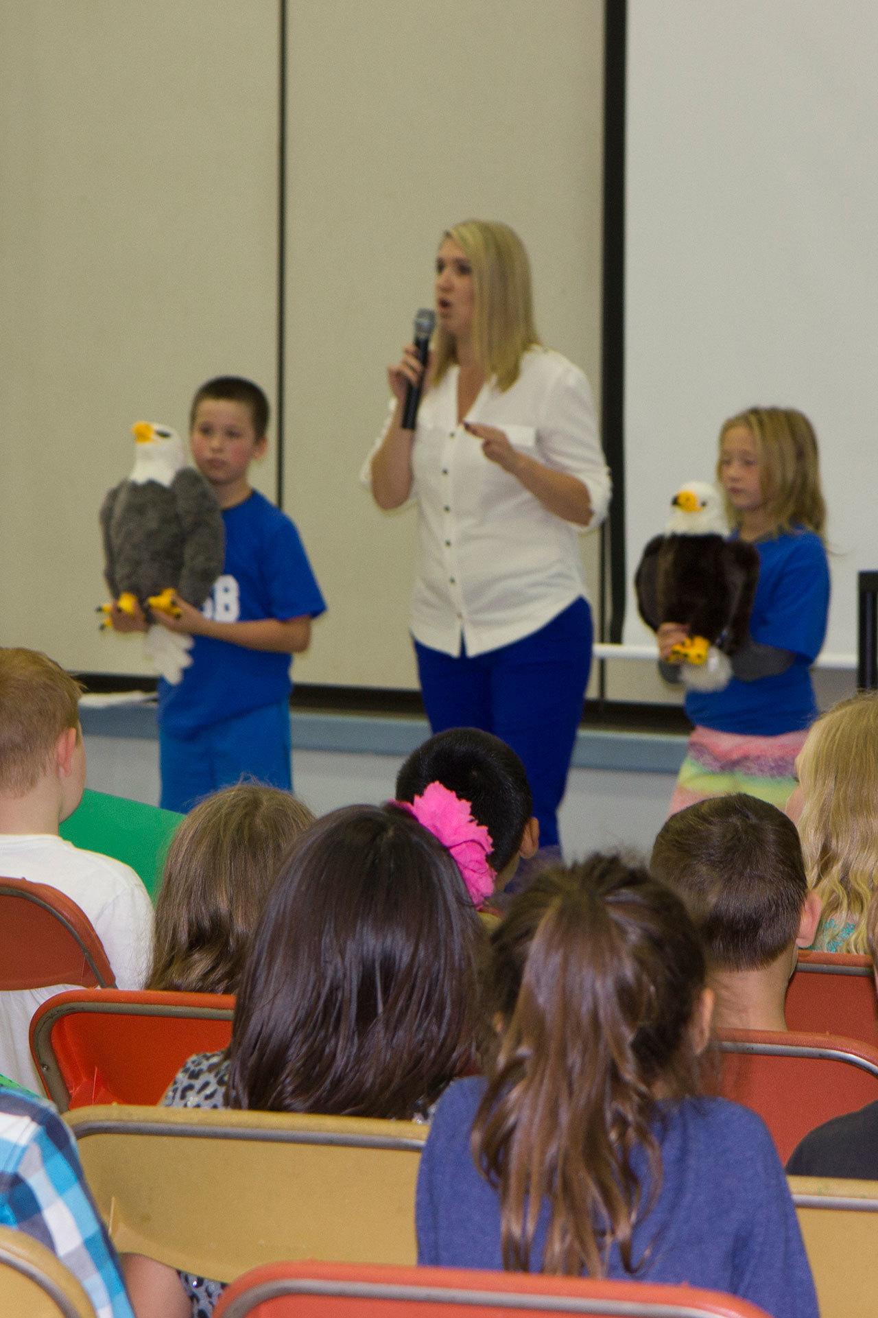 (Stephanie Morton | The Vidette)                                Heather Moore (center), counselor at Elma Elementary addresses the student body at the Make Your Day assembly held on Sept. 26. Fifth-grade student assistants Timothy DeFlyer (left) and Ashlyn Schamber (right) show off the new plush Elma Eagles who will watch over specially selected classrooms.