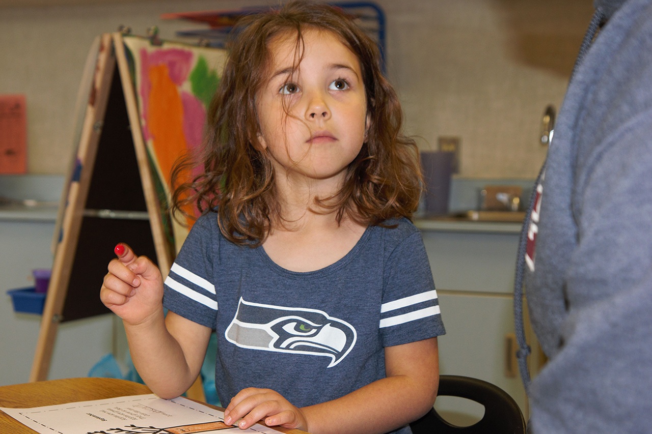 (Stephanie Morton | The Vidette) Makenzie Hart uses her fingertip to paint red apples on a tree as part of an assignment in Ms. Cady’s kindergarten class on Friday.