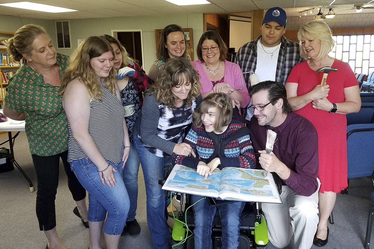 Tommi Halvorsen Gatlin | For The Vidette Where is the Dominican Republic? — (Posed photo) In front, Shaela Burtner, flanked by her parents, Michele and Pastor Aaron Burtner, points to the Dominican Republic on a map. Behind them are, from left, Tammy Antilla, Faith Ramstad, Elizabeth Martinez, Claire Bach, Krista Ramstad, River Johnny and Val Peters. The team, which also includes Shaela’s sister, Janae, will travel to the Dominican Republic next month to serve in various ways with Rick and Tammie Romano, of Mission TwentyFive 35. The hammer, paint brush and roller and work gloves hint they may be doing some construction work.