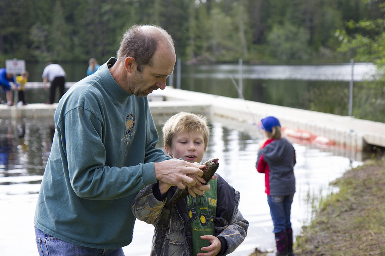 (Corey Morris | The Vidette) Steve Fuchs shows Carter Fuchs, 8, how to hold a fish to pose for a photo during the annual kids fishing derby on June 4 at Panhandle Lake 4-H camp.