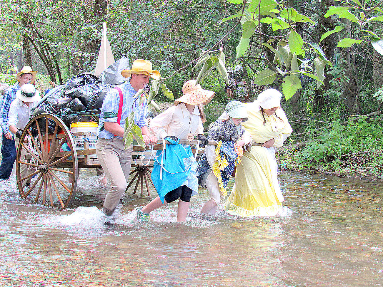 (Photo by KayLynn Larsen) Jared Wallace (left) helps his pioneer family pull a handcart up Big Creek in Cle Elum during the Pioneer Westward Trek Reenactment July 19-22.