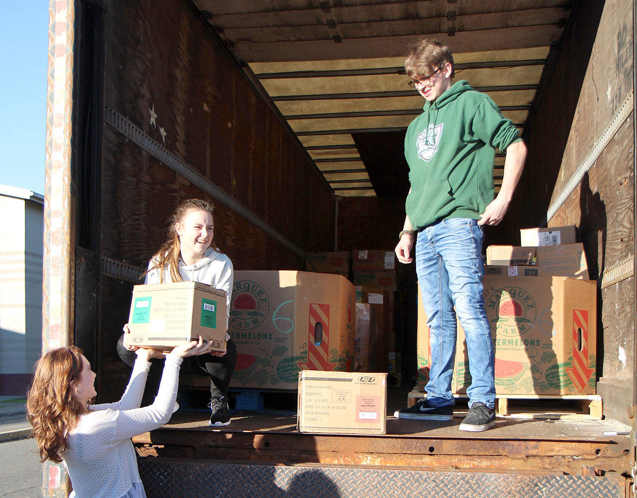 Montesano High School junior Honour Iversen, from left, re-enacts the loading of food with sophomore Cassadie Golding and senior Max Urbanski for the benefit of a photographer who missed the first loading Monday, Dec. 3, 2018, in Montesano. The food was collected for students’ Food Bowl paper bag food drive. There still is an opportunity to give to the food drive. If you have a bag of food to give, you can call the school (360-249-4041) and they will send somebody by to pick it up. Or you can drop it off at the school at 303 N. Church St. Donations also are being accepted online at montesano.revtrak.net. Food and money will go to the Montesano Food Bank.