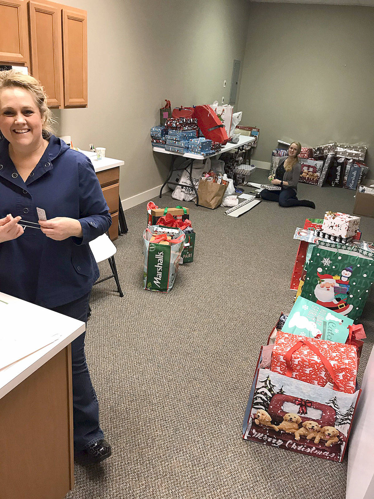 (Courtesy Kyna Wilson) Miriam Jones, owner of Picket Fence Preschool, places gift tags on packages at Hands-on-Health Chiropractic in Montesano. Savanah Jackson, background, a new employee at Hands-on-Health, spent eight hours Dec. 17 wrapping presents.