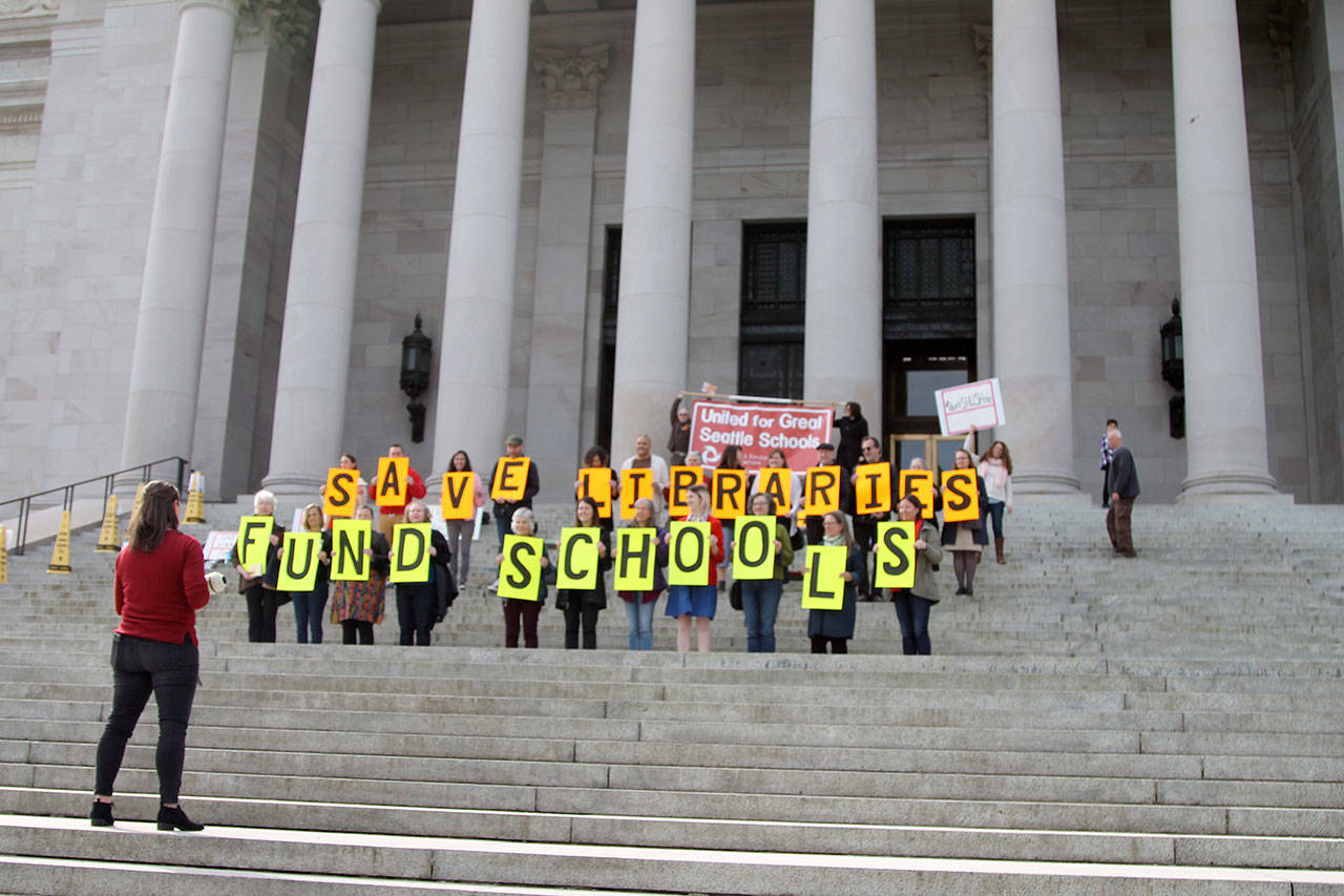 Seattle Public School’s librarians hold up signs on the capitol building steps, in protest of funding cuts that have resulted in cuts to libraries. Kate Eads, who organized the event, can be seen holding a megaphone addressing the group.—Photo by Emma Epperly, WNPA Olympia News Bureau