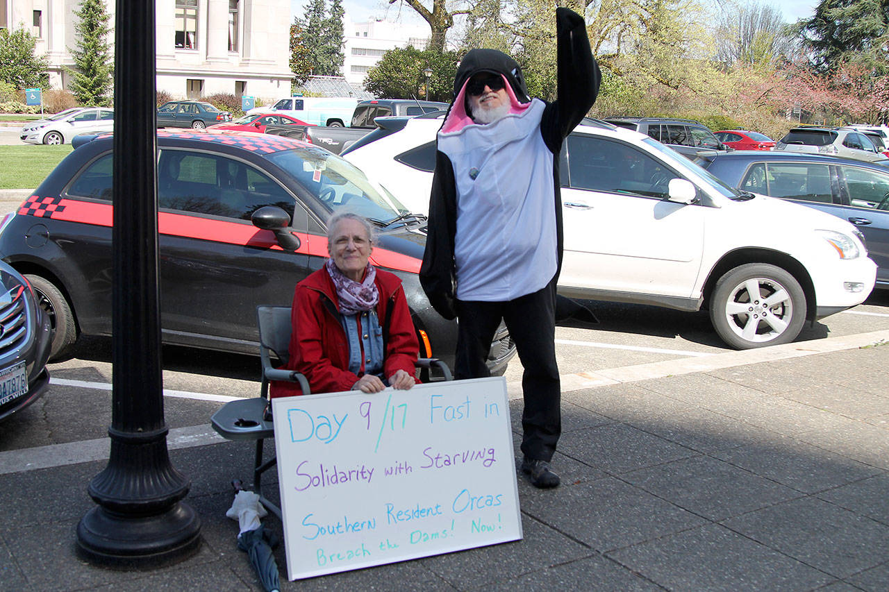 Lanni Johnson sitting in front of the capitol building steps where she has been on a hunger strike for the last 9 days to save the Southern Resident Orcas. Johnson is joined by supporter, Phil Myers, who can be seen in an orca onesie.                                (Emma Epperly | Washington Newspaper Publishers Association)