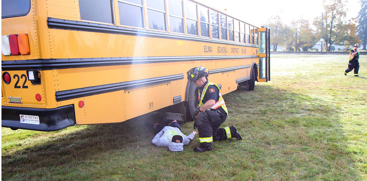 Tysen Richardson pretends to be pinned under a bus during an emergency preparedness drill Wednesday, Oct. 23, in Elma, while an emergency medical technician from Fire District 5 examines him. (Michael Lang | Grays Harbor News Group)