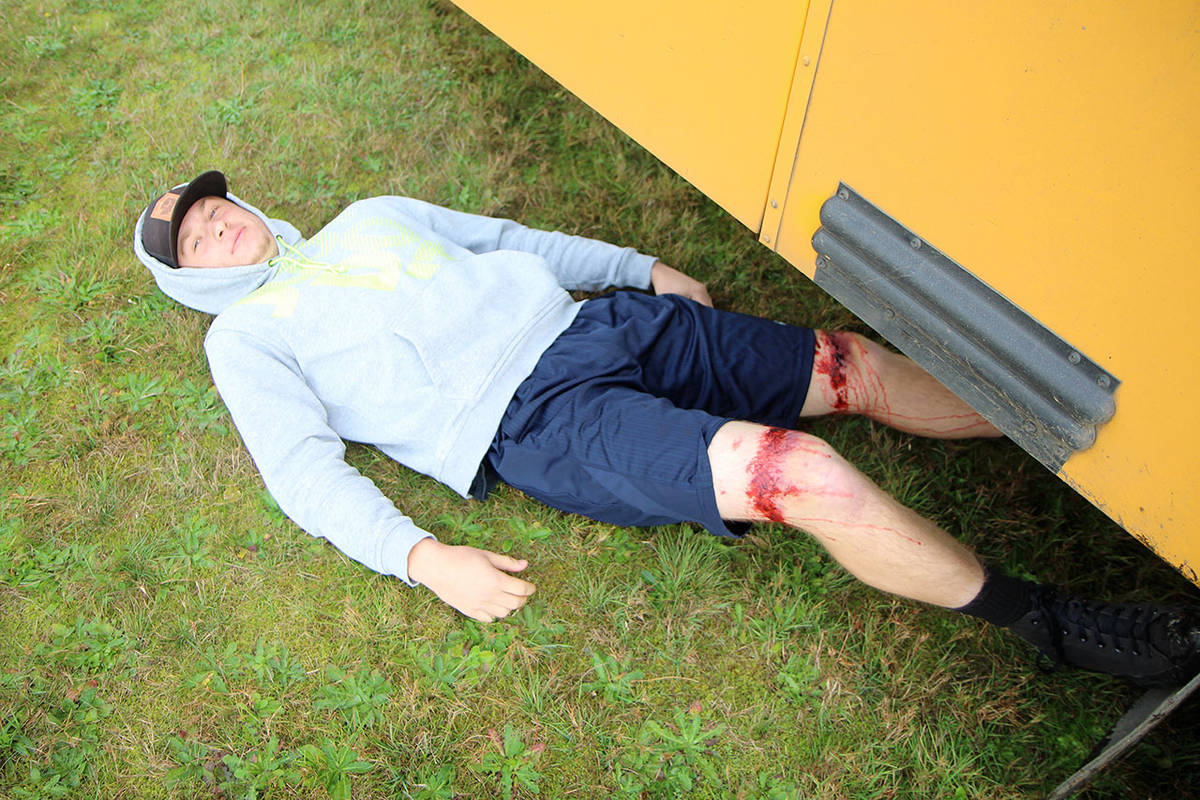 Elma High School senior Tysen Richardson pretends to have been thrown from a roll-over bus accident and pinned beneath the vehicle Wednesday, Oct. 23, during an emergency preparedness drill at the Grays Harbor Fairgrounds in Elma. His legs have makeup on them to make the simulation more lifelike. Richardson and other “victims” of the crash were transported to Summit Pacific Medical Care by first responders for additional aid. (Michael Lang | Grays Harbor News Group)