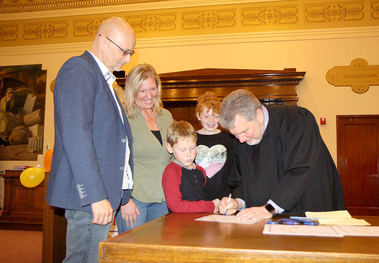 Judge Stephen Brown (right) signs an adoption certificate as Sean (from left) and Terri Robles adopt Eric and Julianna on Friday during the National Adoption Day ceremony at Grays Harbor County Superior Court in Montesano. (Michael Lang | Grays Harbor News Room)