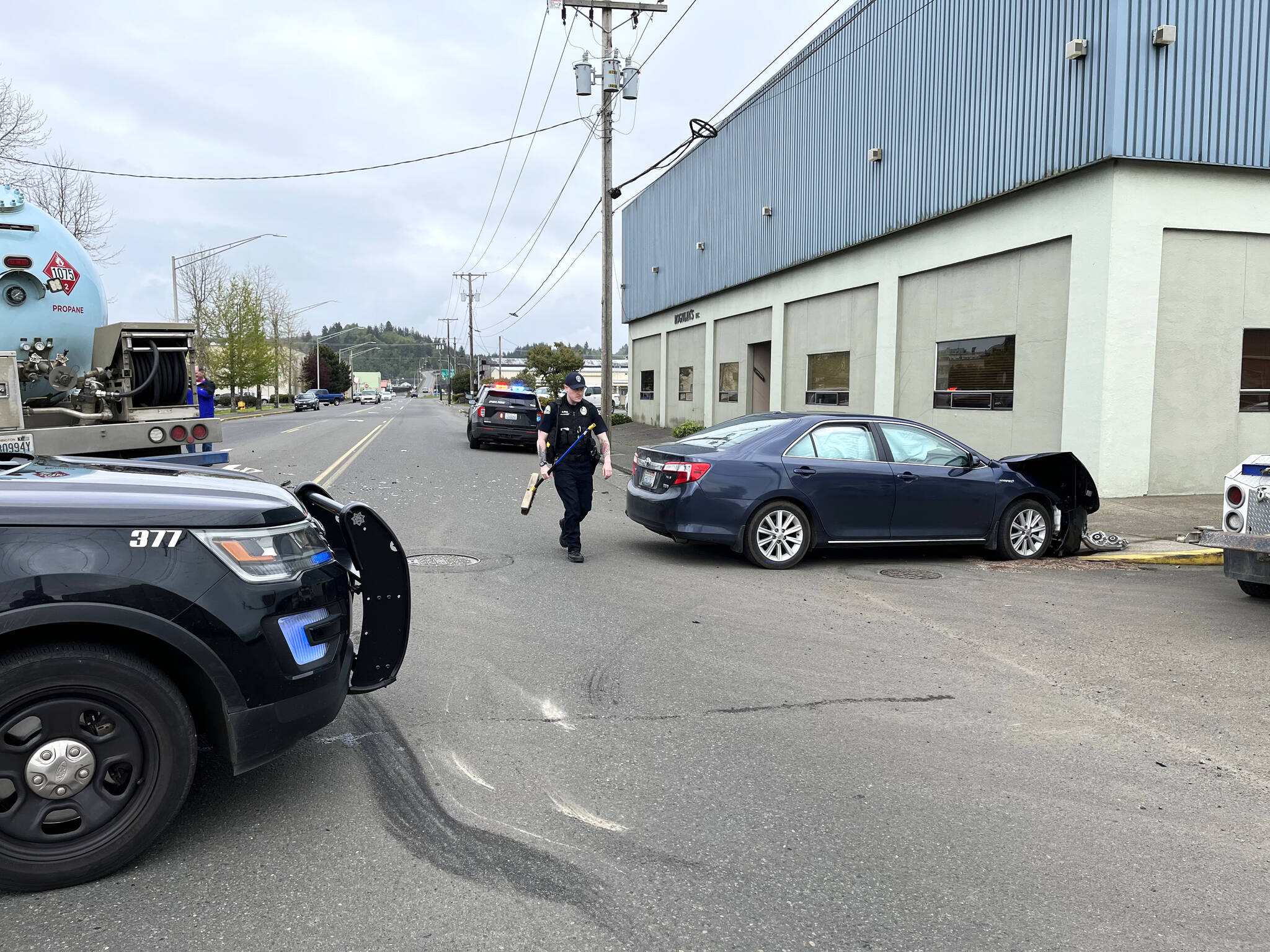APD Patrol Officer Stephen Ayers carries a push broom to help him clear the debris from the 3-car collision Wednesday afternoon, May 18, at the intersection of South M Street and West State Street in Aberdeen. Matthew N. Wells | The Daily World