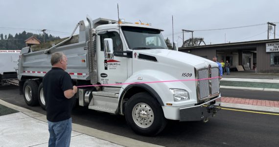 (Matthew N. Wells | The Daily World)
                                Aberdeen Mayor Pete Schave drives a Rognlin’s Inc. dump truck through the new roundabout just after 12 p.m., on Wednesday, Sept. 14. Rick Sangder, public works director for the city of Aberdeen, left, held the left end of the pink ribbon. City Engineer Nick Bird held the right end of the ribbon. The roundabout replaces the former five-way intersection of East Market Street, F Street and the one-way street, Fuller Way.