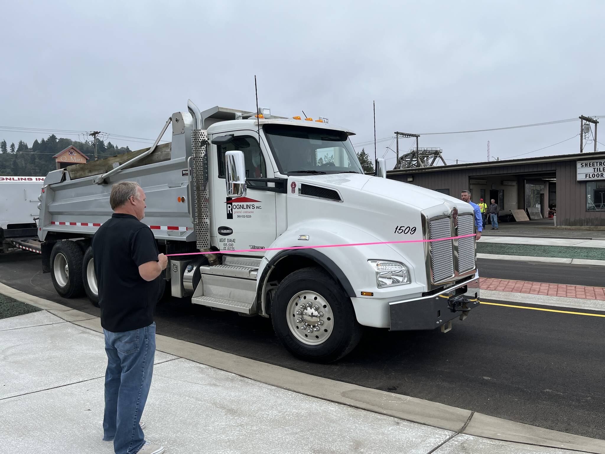 (Matthew N. Wells | The Daily World)
                                Aberdeen Mayor Pete Schave drives a Rognlin’s Inc. dump truck through the new roundabout just after 12 p.m., on Wednesday, Sept. 14. Rick Sangder, public works director for the city of Aberdeen, left, held the left end of the pink ribbon. City Engineer Nick Bird held the right end of the ribbon. The roundabout replaces the former five-way intersection of East Market Street, F Street and the one-way street, Fuller Way.